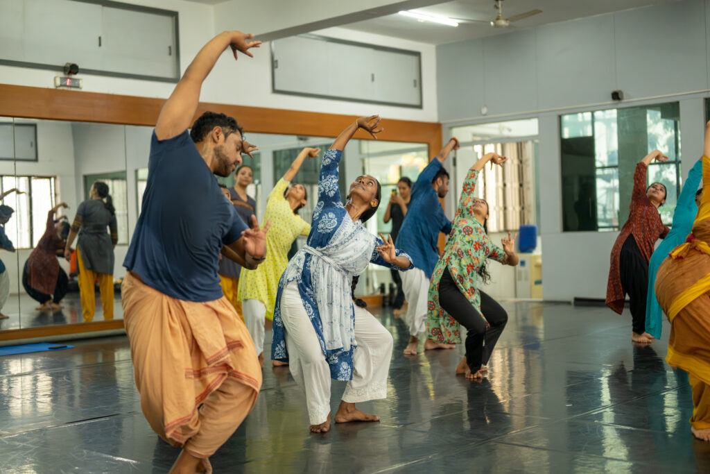 Several dancers in a studio stretching over to one side.