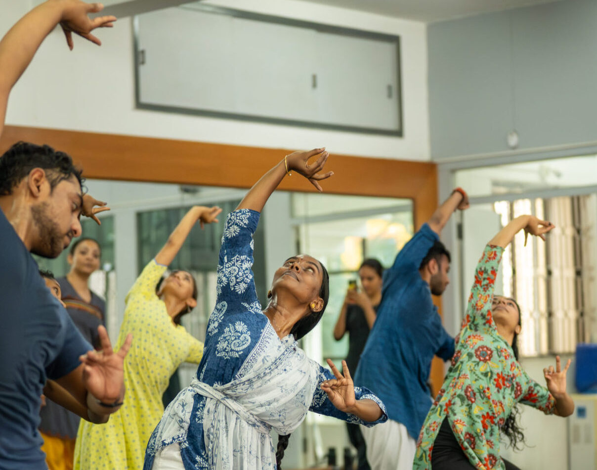 Several dancers in a studio stretching over to one side.