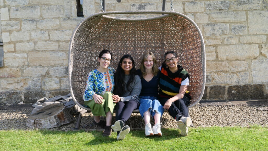 Four females including artistic director Seeta Patel, sitting outside on a floating wicker chair, smiling.
Photo Credit: Ian Abbott